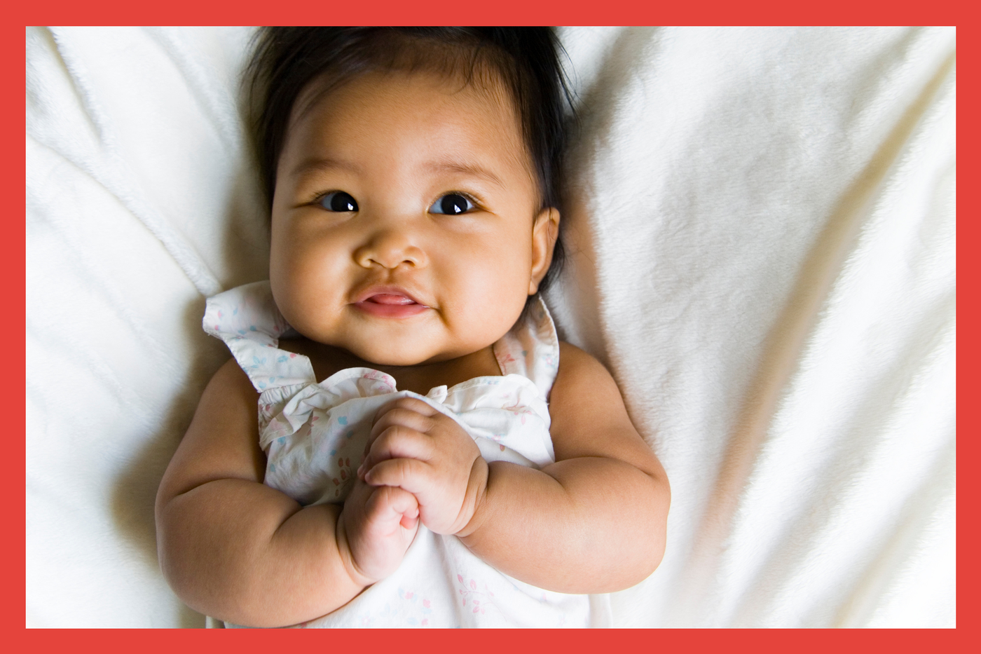 Baby girl laying on blanket holding her hands and smiling. 